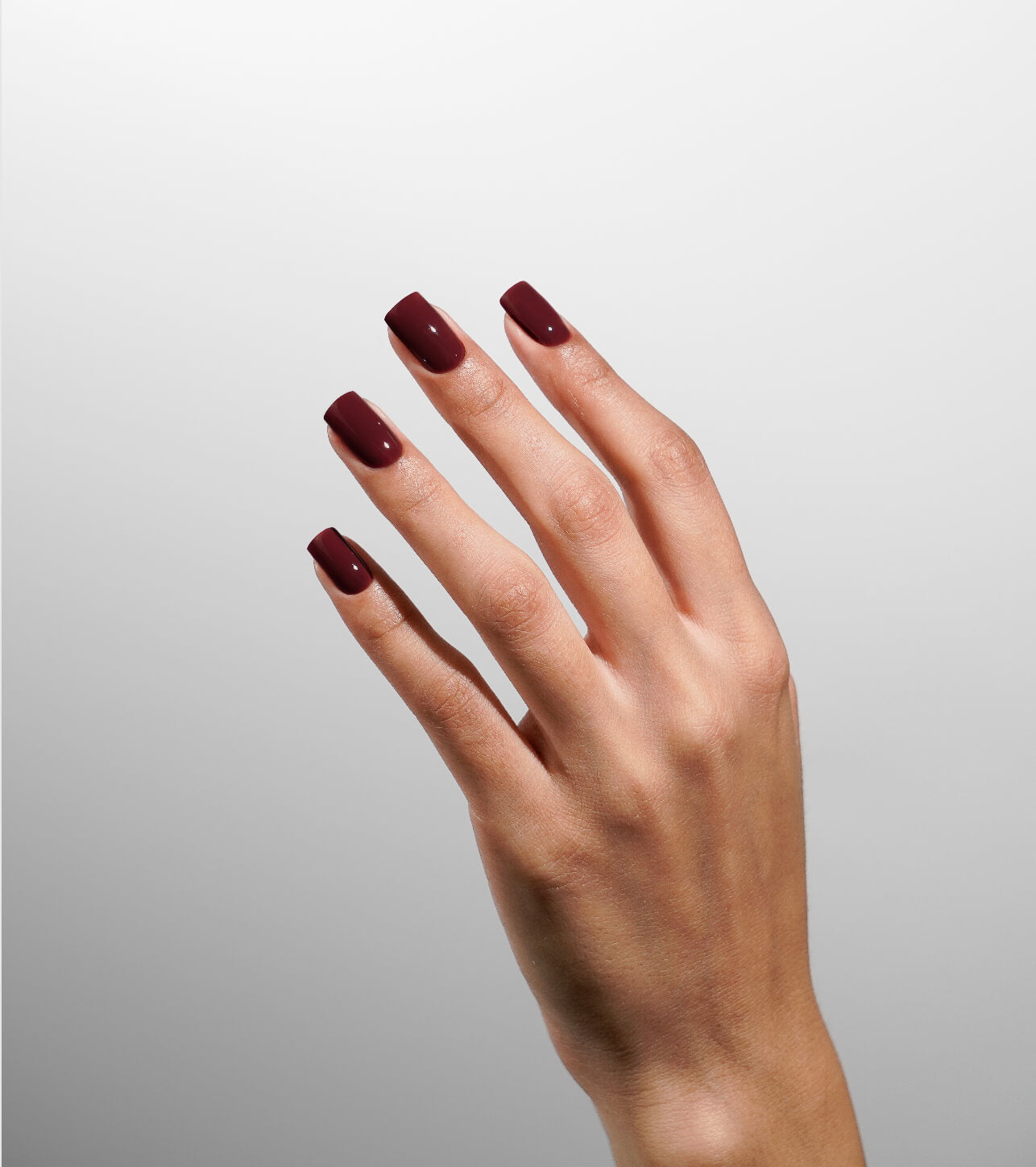 Hand with burgundy nail polish on a light gray background