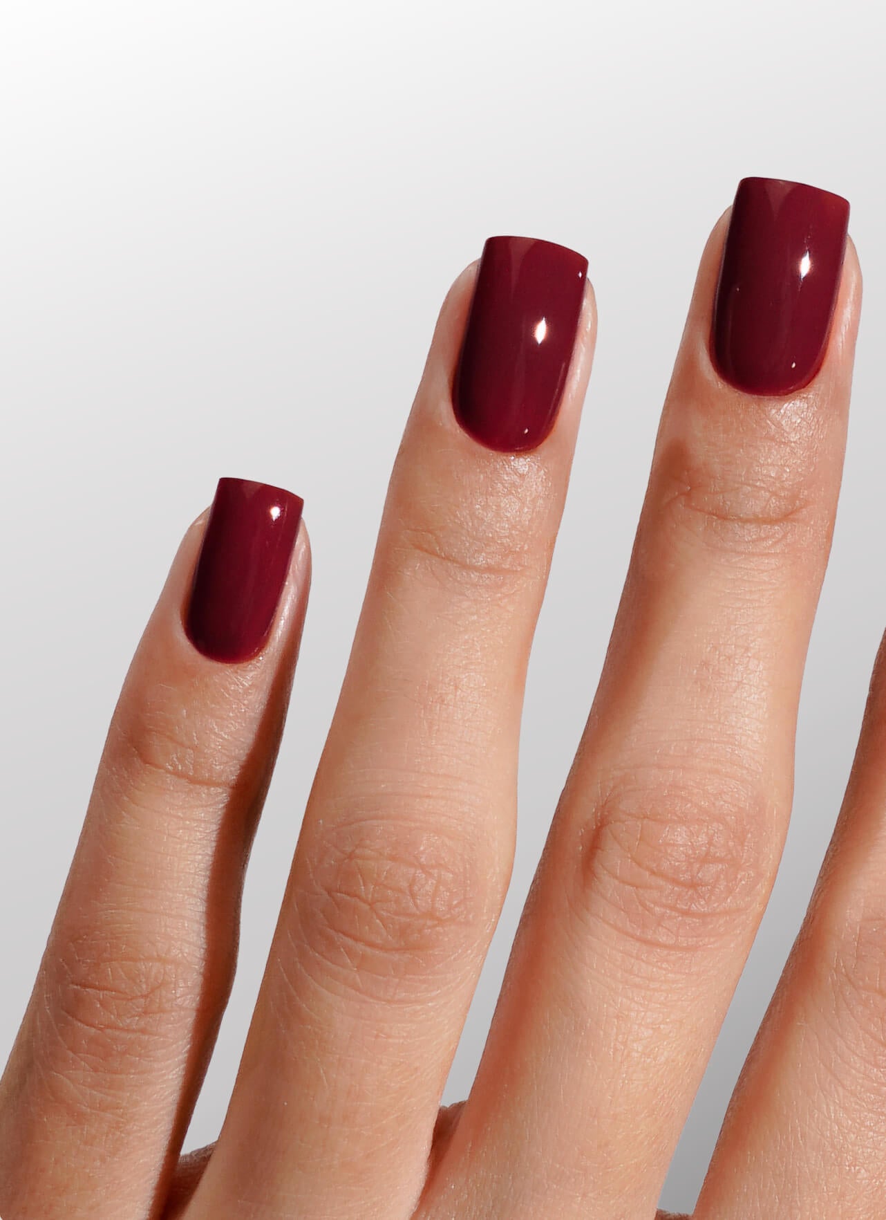 Close-up of a hand with burgundy nail polish on a light gray background
