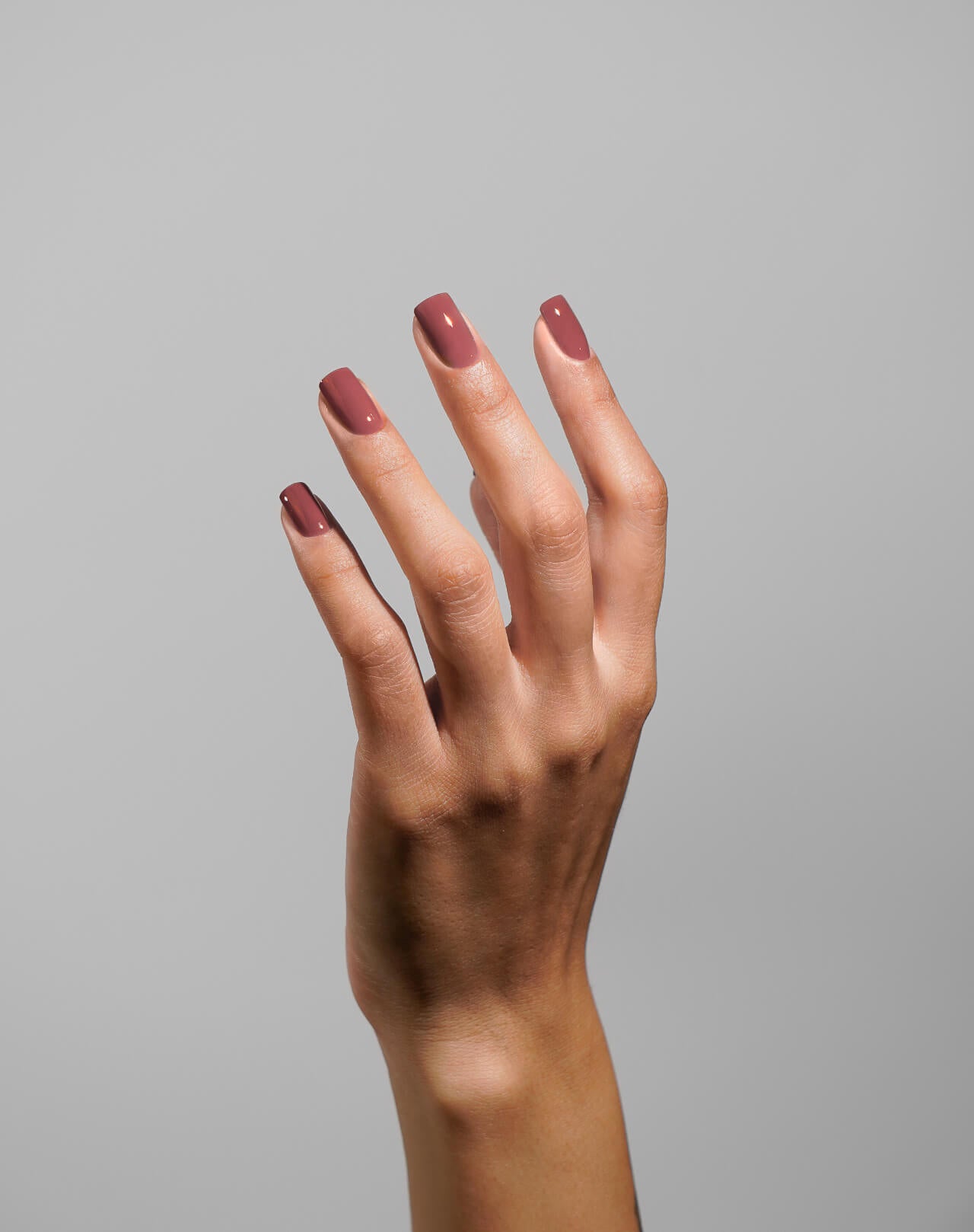 Hand with maroon nail polish on a gray background