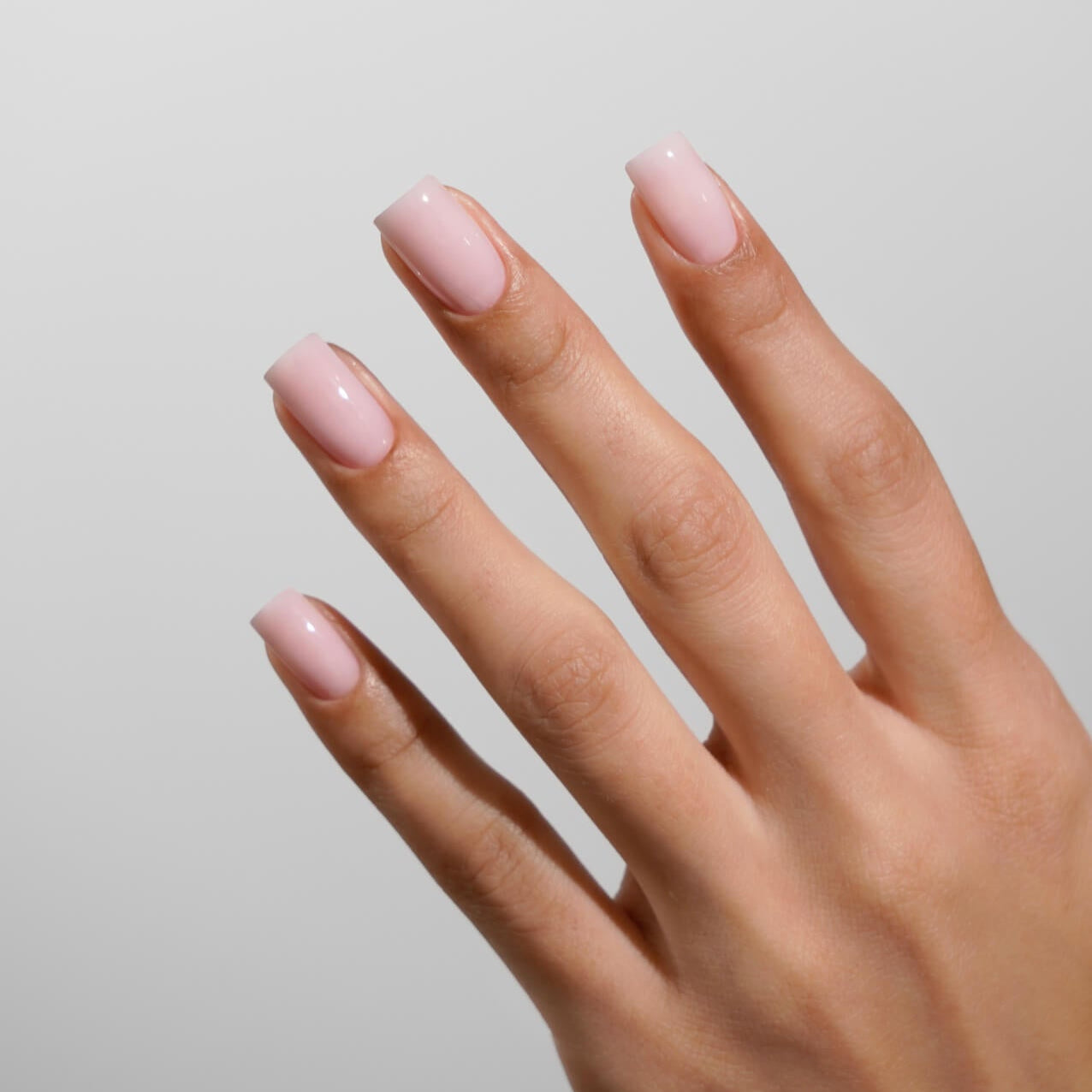 Hand with pink nail polish on a plain background