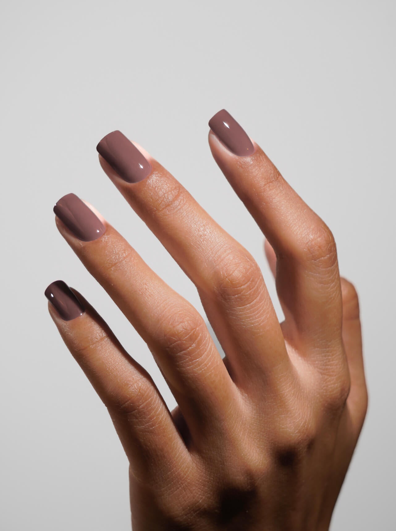 Hand with brown nail polish on a plain background